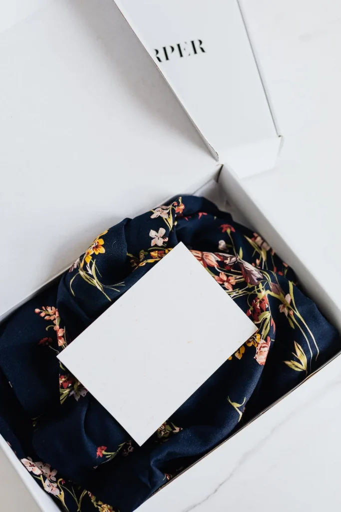 A box with a piece of clothing and a small white piece of paper on top that a customer received from a subscription service through recurring payments.