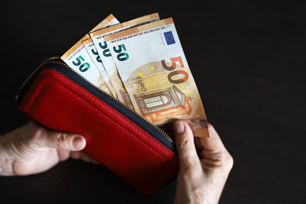 A person pulling euros out of a red wallet to make a payment in Spain to a merchant.