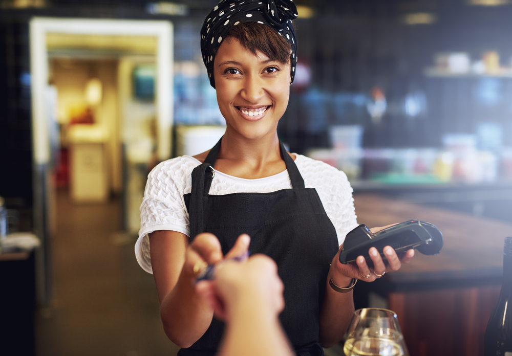 Smiling waitress or small business owner taking a credit card from a customer to process.