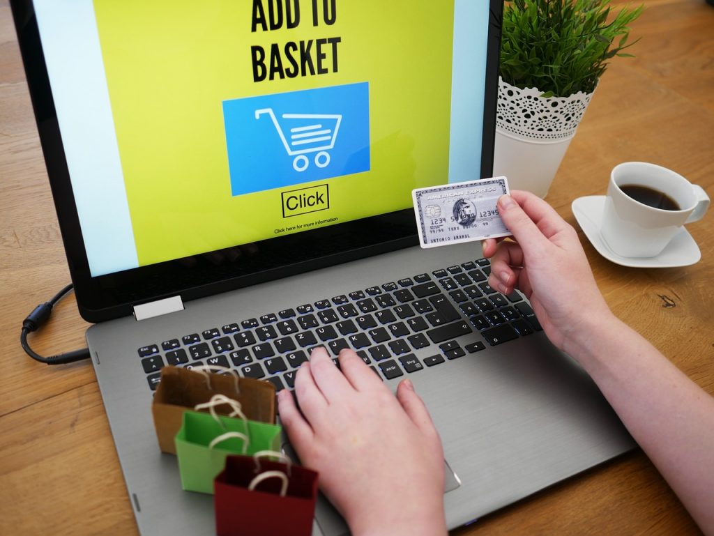 A picture of a person holding a bank card in front of a laptop with a screen reading "Add to Basket". 