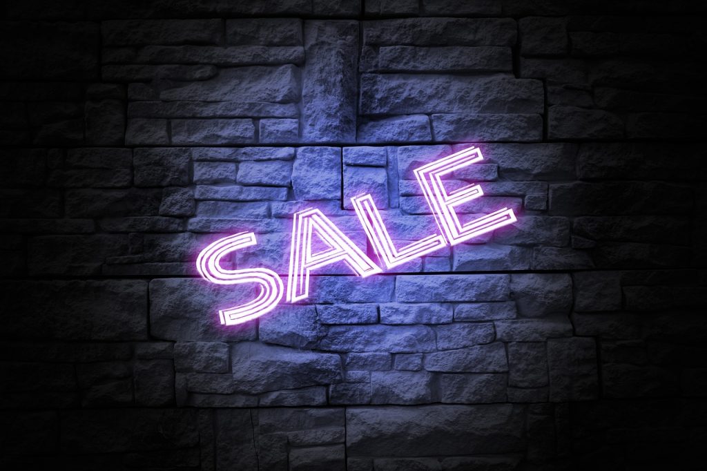 A neon sign reading “Sale” in front of a brick wall.