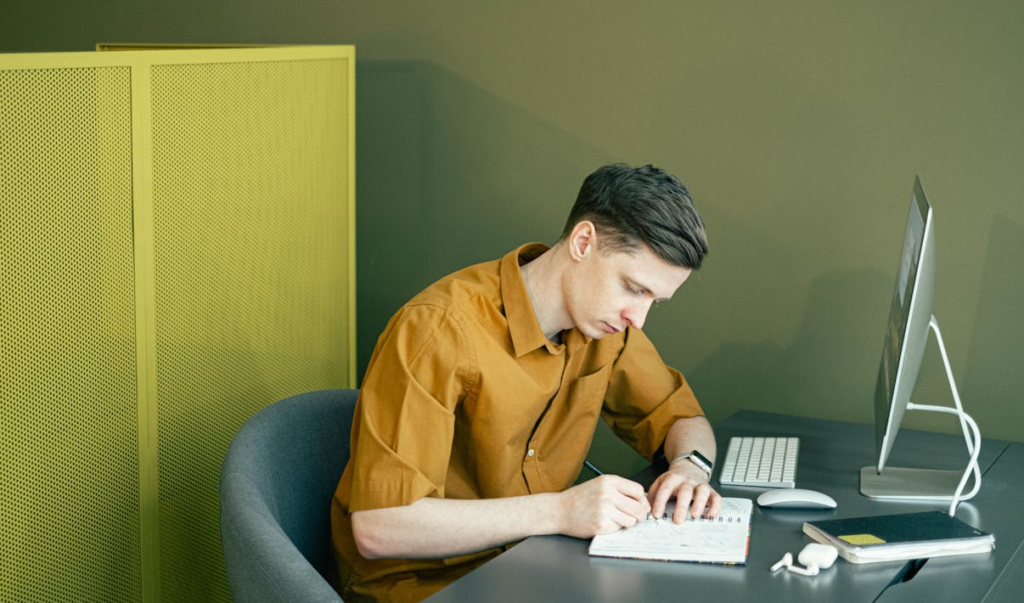 Man sitting at a desktop computer writing notes