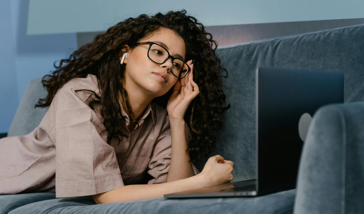 Woman wearing glasses on her sofa looking at her laptop while thinking